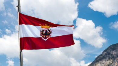 Austrian flag with a pole and rope on a blue sky with clouds and mountain
