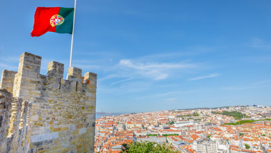 Lisbon aerial cityscape from Sao Jorge Castle on highest hill in Alfama. Waving portuguese flag on top of Lisbon Castle a popular tourist attraction. Panoramic view skyline of downtown on Tagus River.