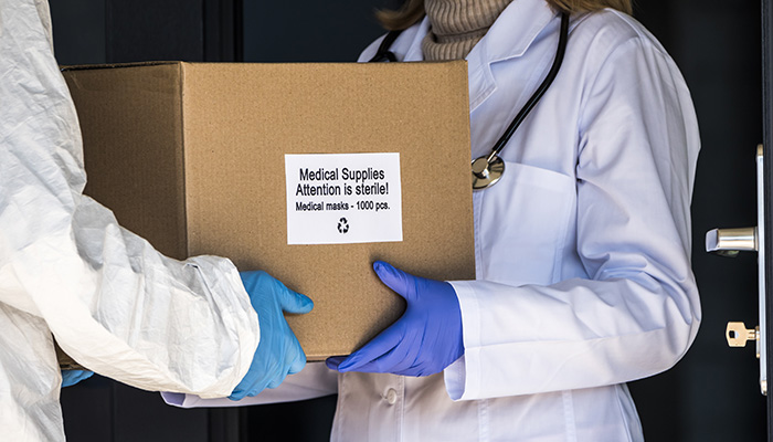 A person in a protective suit is handed a box with protective medical masks to the doctor.