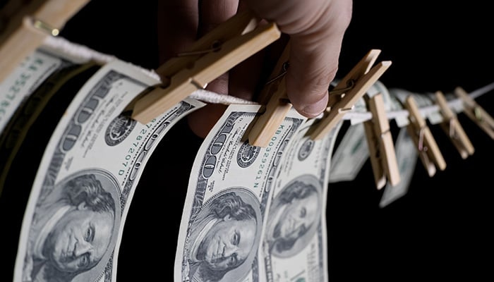 man's hand hangs dollars on a black background using clothespins on a rope. concept of dirty money.
