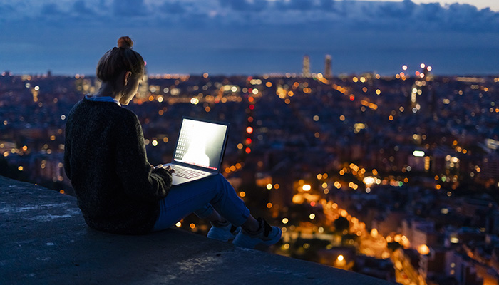 Young woman using laptop at dawn above the city, Barcelona, Spain