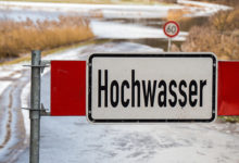 Road barrier with flood warning sign in front of flooded road in germany