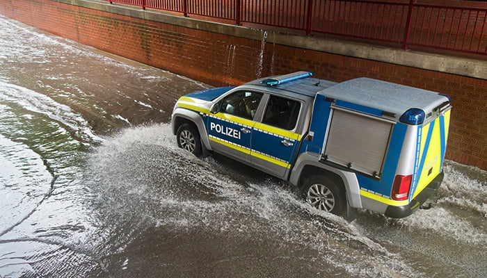 Brake, Germany - July 14, 2021: a vehicle of the water police drives through the railroad underpass flooded after a cloudburst - water splashes