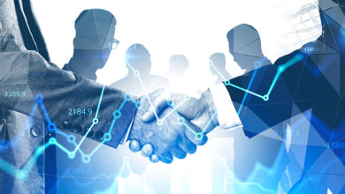 Two businessmen shaking hands in abstract city with double exposure of blurry diverse business people and financial graphs. Concept of partnership and stock market. Toned image