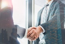 Double exposure of two businessmen reaching an agreement and making handshake with abstract construction building - Greeting and dealing real estate business concepts.