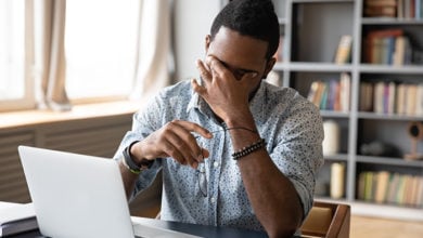 Tired african American male worker take off glasses massage eyes suffer from headache or migraine at workplace, exhausted biracial man have blurry vision overwork at laptop, health problem concept