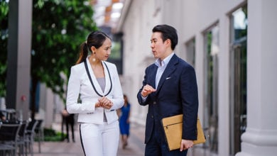 Portrait of two young, confident and attractive Asian business people standing in a city during the day. They are both professionally dressed in suits and are smiling as they talk to one another. ; Shutterstock ID 1450298177