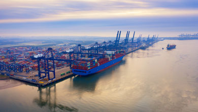 Aerial photograph of Felixstowe container port in the early morning autumn mist, a cargo ship being loaded, rows of stacked multi-colored containers, and loading gantries stretching off into the mist