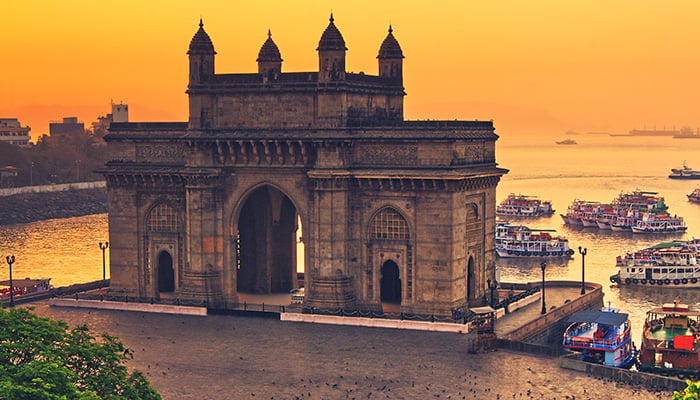 The gateway of India at sunrise with beautiful reflections in the sea. Boats in the water in a hot day.
