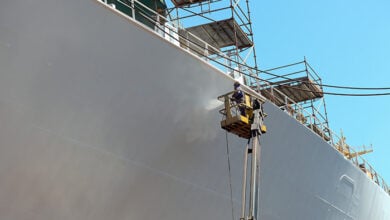 Worker painting ship hull using airbrush.