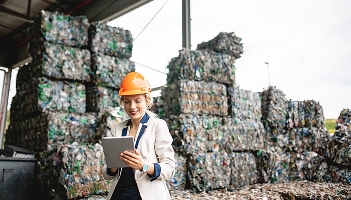 Close-up of female environmental expert using digital tablet for notes while conducting satisfying onsite inspection of recycling facility.