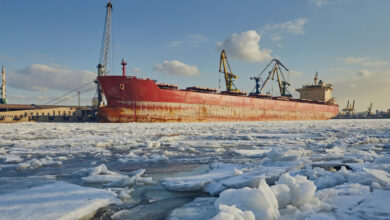 Cargo ship in the port in winter, against the background of ice, snow and blue sky