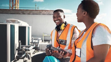 Stock image of Black man and women in hi-vis jackets on a building site.